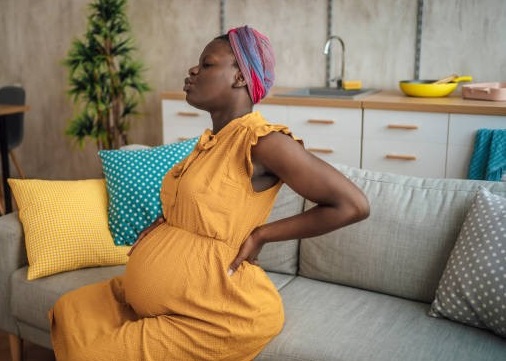 A black pregnant woman in a yellow gown sitting on a couch