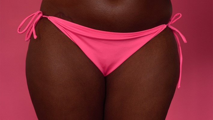 A standing black woman's lower torso in a pink bikini