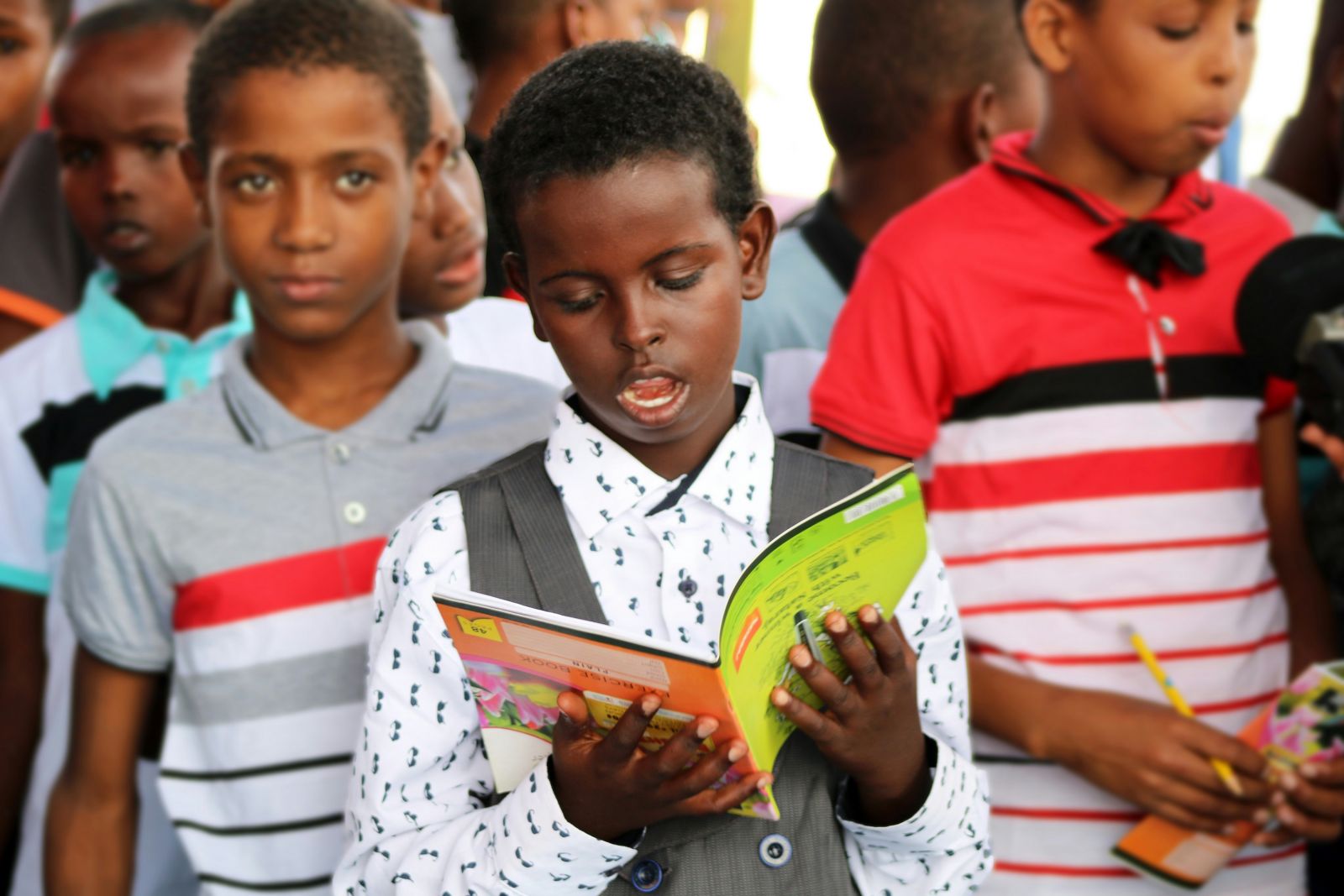 An African child reading a book in school with peers in attention