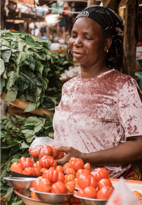 African woman vegetable seller holding tomatoes and leafy vegetables