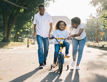 Black couple spending time outdoor teaching their child to learn how to ride a bicycle.