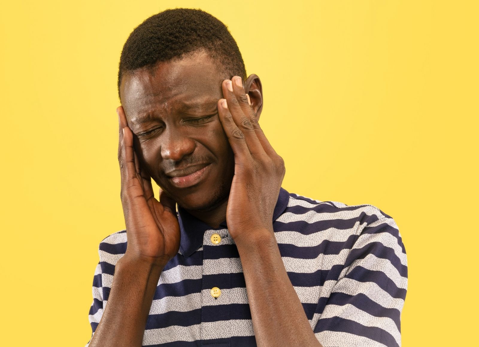 A black man looking distressed and holding his head in his hands suggesting a headache