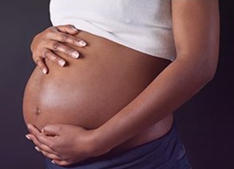 A black pregnant woman holding her bulging abdomen in her hands.