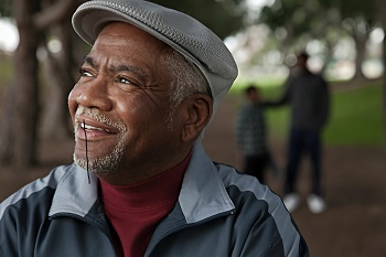 A happy looking elderly black man wearing a cap and looking into the horizon