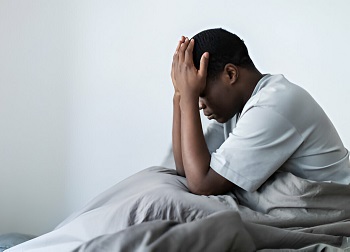 An African man sitting in his bed with his head in both hands