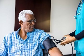 A healthcare provider checking the blood pressure of an elderly African man