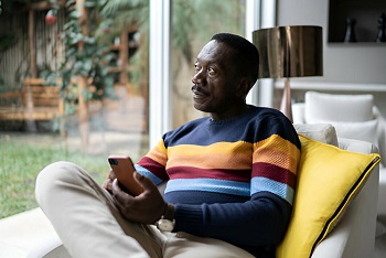  An African man sitting on a sofa and staring out of a glass window