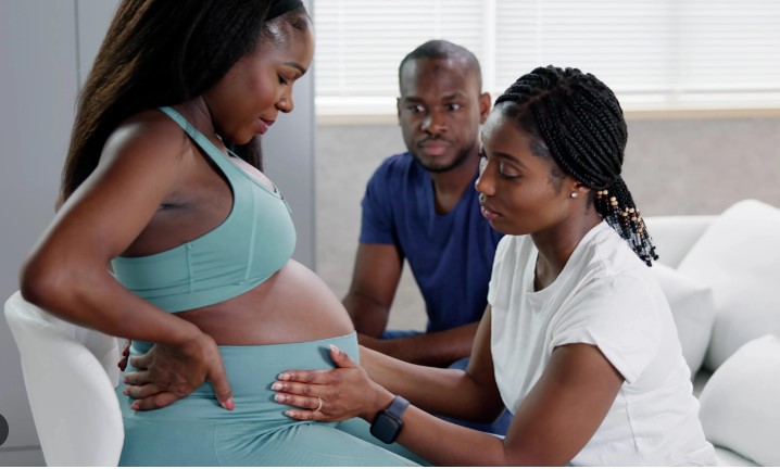 A black pregnant woman and nurse at antenatal care with male partner looking on