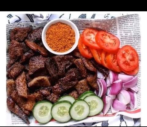 Nigerian skewered meat (Suya) and vegetables in a newspaper wrap with with a small bowl  of spices