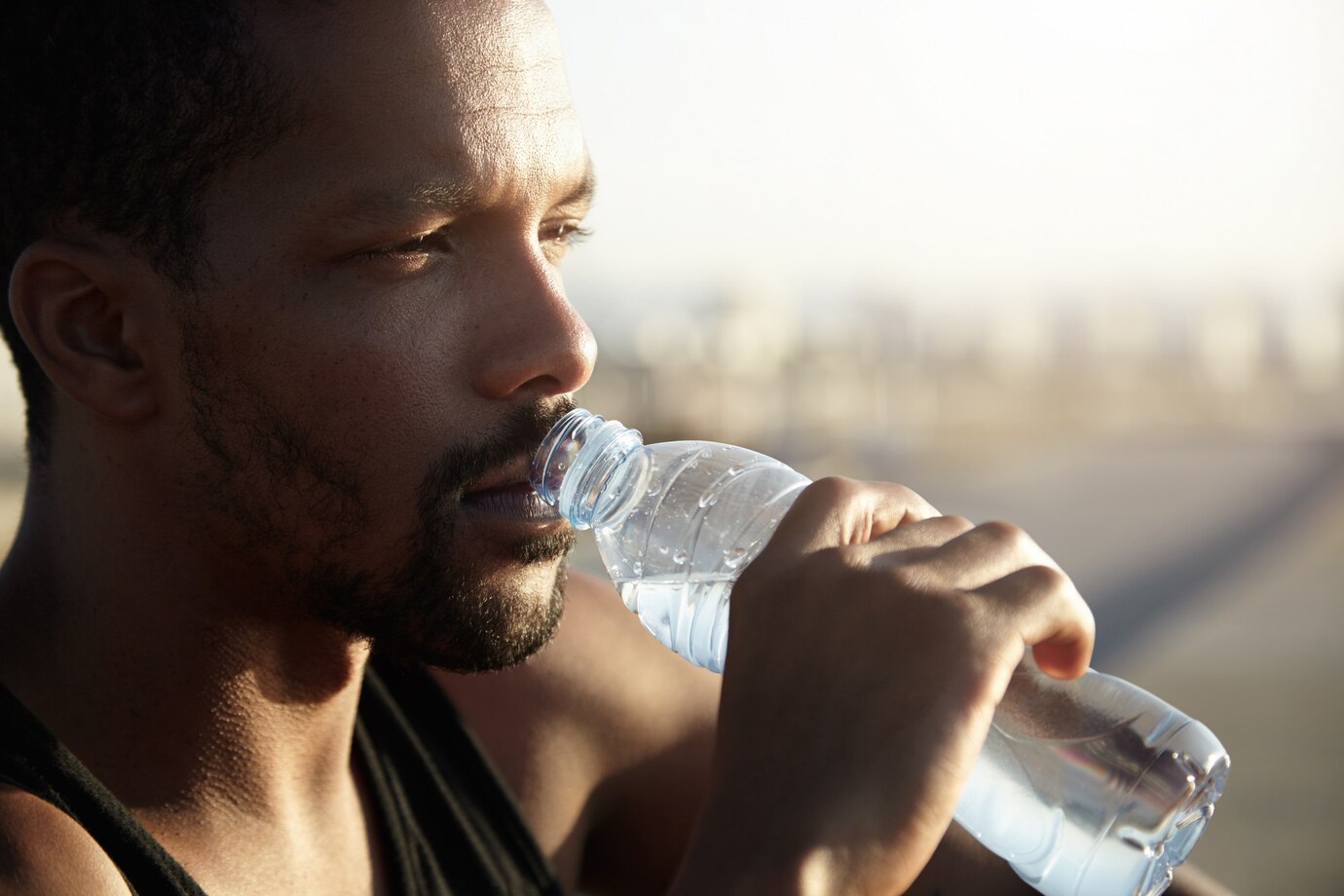 An adult black male standing and drinking water from a bottle