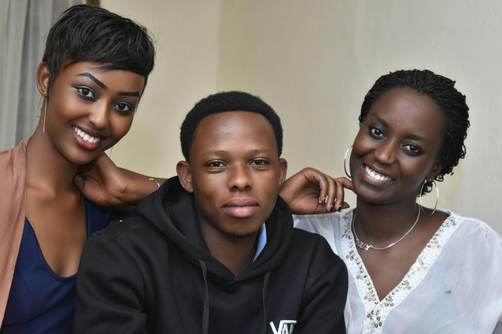 Three young African adults, smiling and posing together indoor.