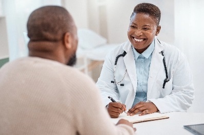 A seated black patient talking with a smiling young black doctor.