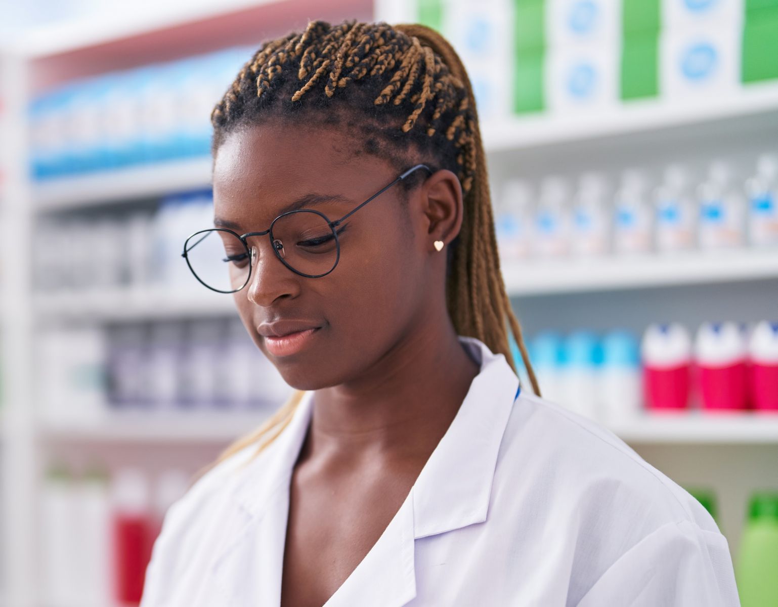 A young black female pharmacist standing at work with serious expression