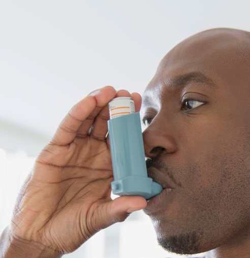 A black man using an inhaler