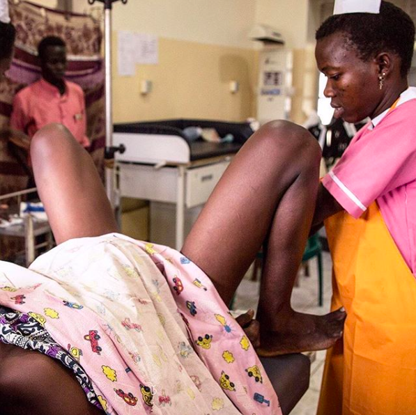 A black woman lying in bed and  in labour attending by a nurse