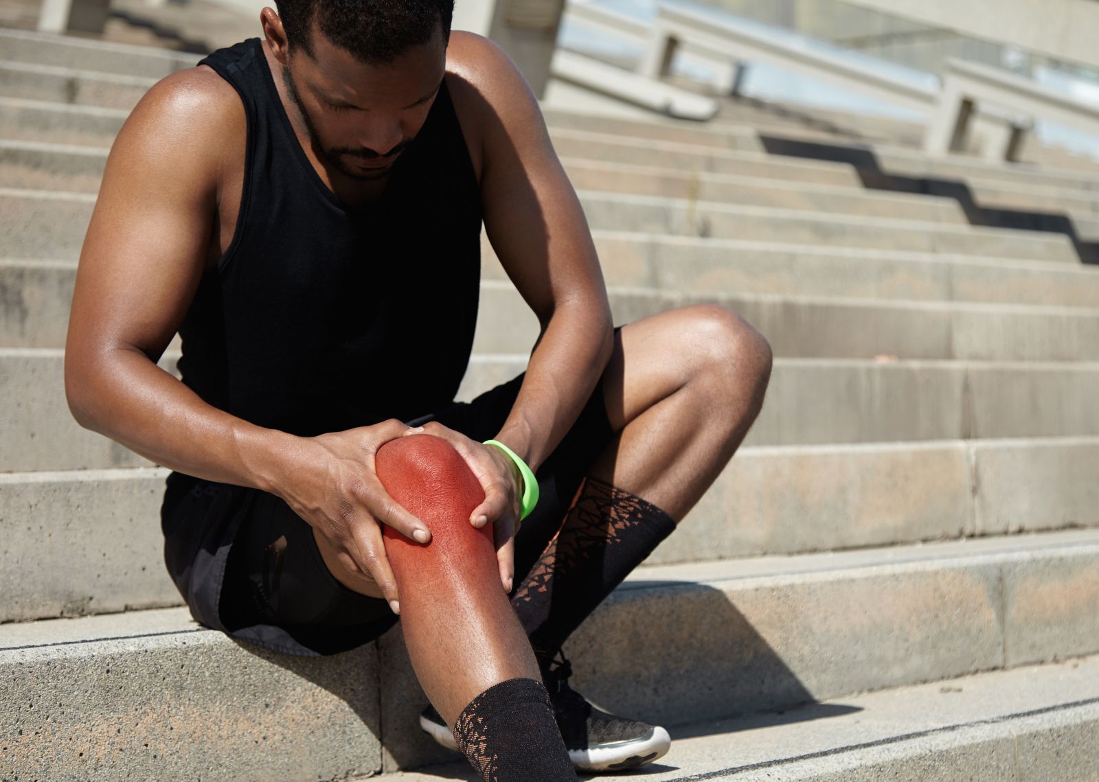 A black runner holding his swollen, red and painful right knee in both hands