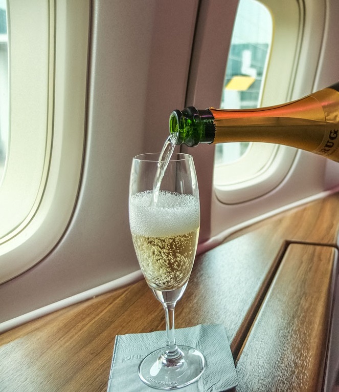 Sparkling wine being served from a bottle into a drinking glass on an airplane cabin
