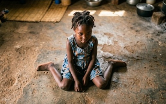 Photo of an African child in W sitting on a bare floor