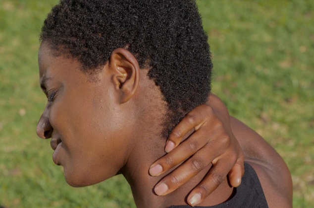 A young black lady looking distressed and in pain, holding the left side of her neck