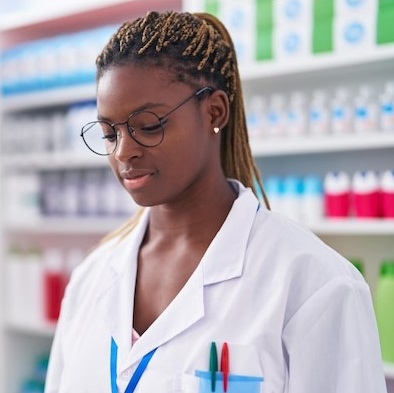 A young black female pharmacist standing at work with serious expression.