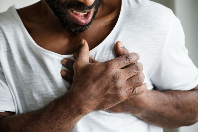An African man wearing a white T-shirt, clutching his chest in discomfort
