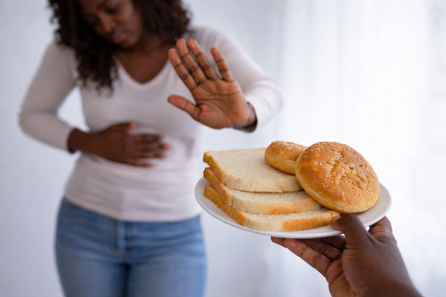 An African woman holds on to her abdomen in apparent pain while rejecting a plate of bread offered by another a hand.